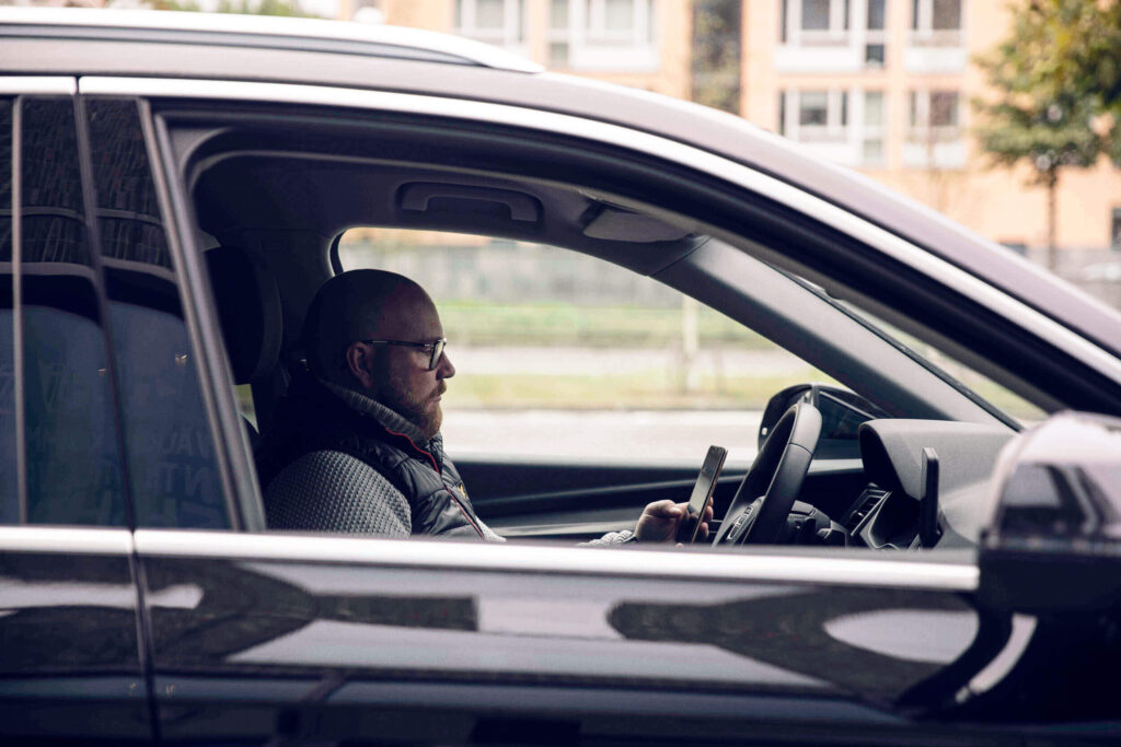 Sjåfør i bil bruker mobil for digital kjørebok.