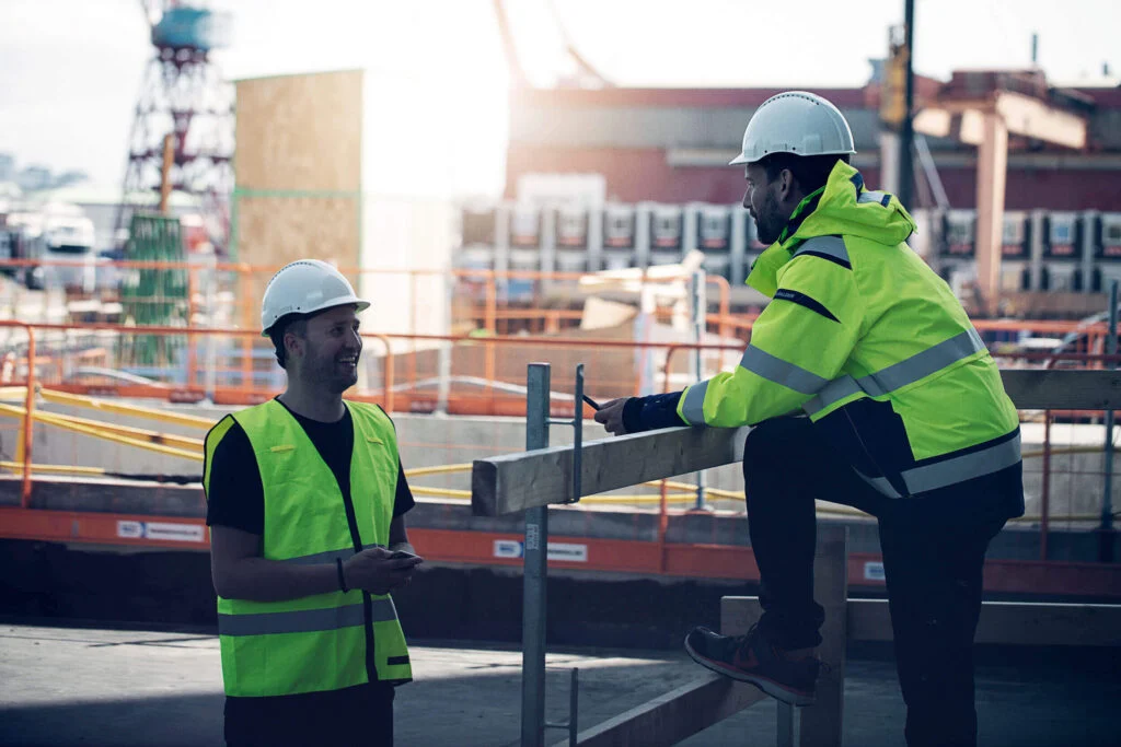 To arbeidere i verneutstyr på byggeplass – digital registrering og onboarding med Infobric.