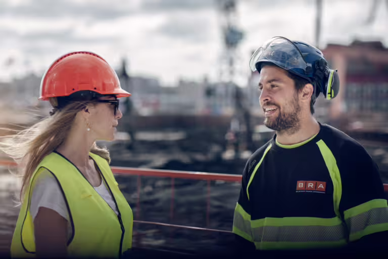 byggarbetare med orange och svart hjälm pratar på byggarbetsplats